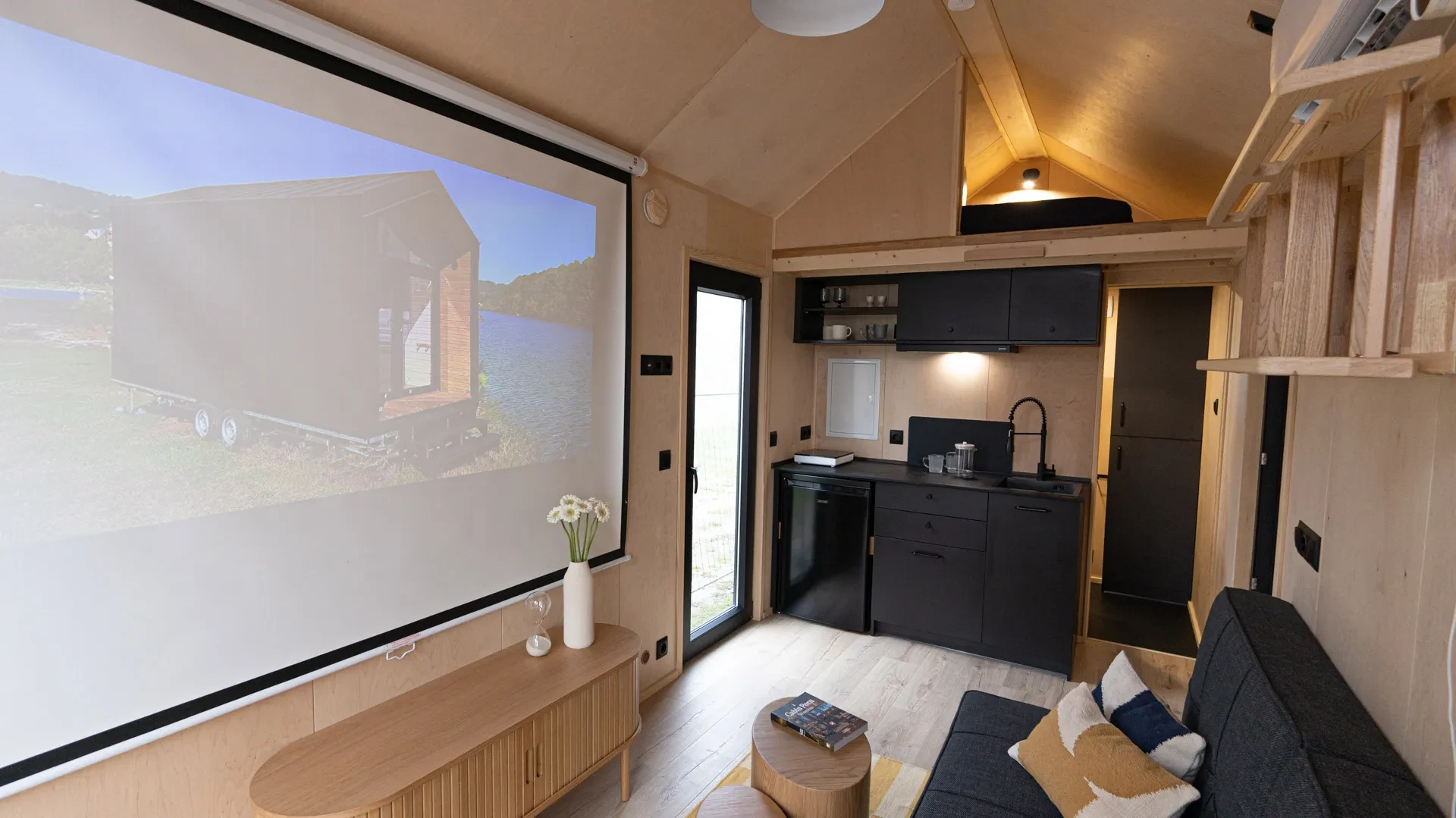Wohnbereich mit Leinwand, Küchenzeile und Schlafempore